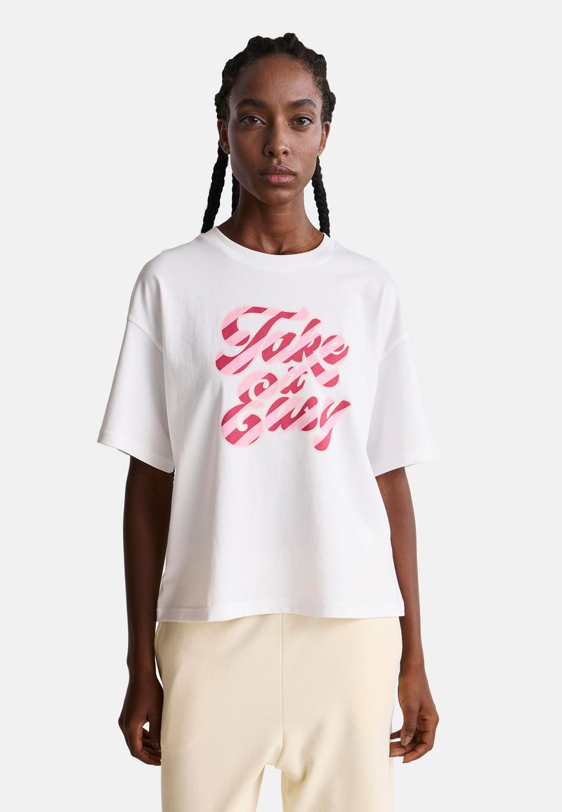 Camiseta de algodón blanca de manga corta, con un gráfico en negrita de color rosa que dice "Tómalo con calma" en diseño a rayas. Corte relajado con cuello redondo.