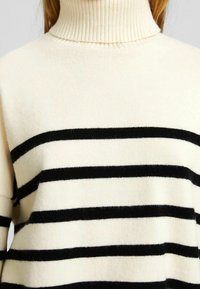 Rollkragenpullover in Creme mit schwarzen horizontalen Streifen, aus weichem Strickmaterial. Verfügt über einen gerippten Ausschnitt und eine lockere Passform.