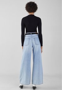 Jean denim bleu clair à jambes larges et taille haute, associé à un haut noir côtelé. Comprend des poches arrière et un dégradé de lavage clair.