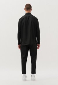 Camicia nera con bottoni e pantaloni attillati, entrambi in un tessuto morbido. L'outfit presenta un design minimalista ed è abbinato a sneaker bianche.