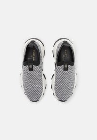 Slip-On Sneakers mit einem strukturierten Strick-Obermaterial in Schwarz und Weiß, einer gepolsterten weißen Sohle und einem schwarzen Zugband mit Logo-Detail.