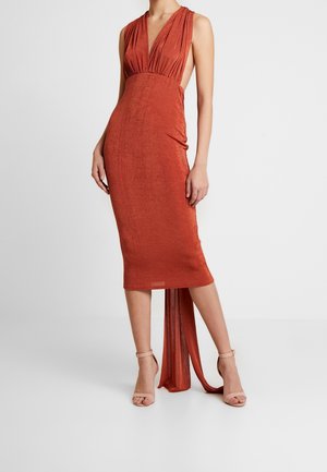 Bezrękawnikowa rustykalna sukienka midi z głębokim dekoltem w kształcie litery V, otwartymi bokami i marszczonym materiałem na plecach, noszona z beżowymi szpilkami na kostkę z paskiem.