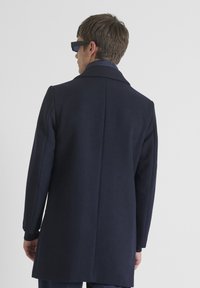 Abrigo de lana navy con una silueta estructurada, solapa con muesca y puños acanalados. La vista posterior presenta un diseño de costura limpio.