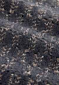 Tissu tricoté gris foncé avec motif texturé en relief et petits détails de fils beiges et blancs créant un motif floral subtil.