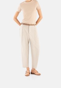 Beige T-Shirt, cremefarbene, plissierte Hose und hellbraune Lederschuhe mit durchbrochenen Akzenten. Das Outfit wird durch einen Gürtel ergänzt, der zu den Schuhen passt.