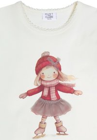 Maglietta bianca a maniche lunghe con una ragazza in abbigliamento invernale, cappello rosso con pon-pon, sciarpa rosa e gonna di tulle grigia, che pattina sul ghiaccio.