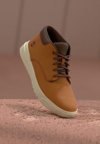 Botín de cuero marrón hasta el tobillo con diseño de cordones, suela de goma color crema, cuello acolchado marrón y forro interior texturizado. Detalle del logo de Timberland.