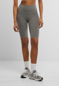 Graue, hoch taillierte Radshorts aus dehnbarem Material, mit glatter Textur und kontrastierenden Nähten. Kombiniert mit grauen Sneakers.