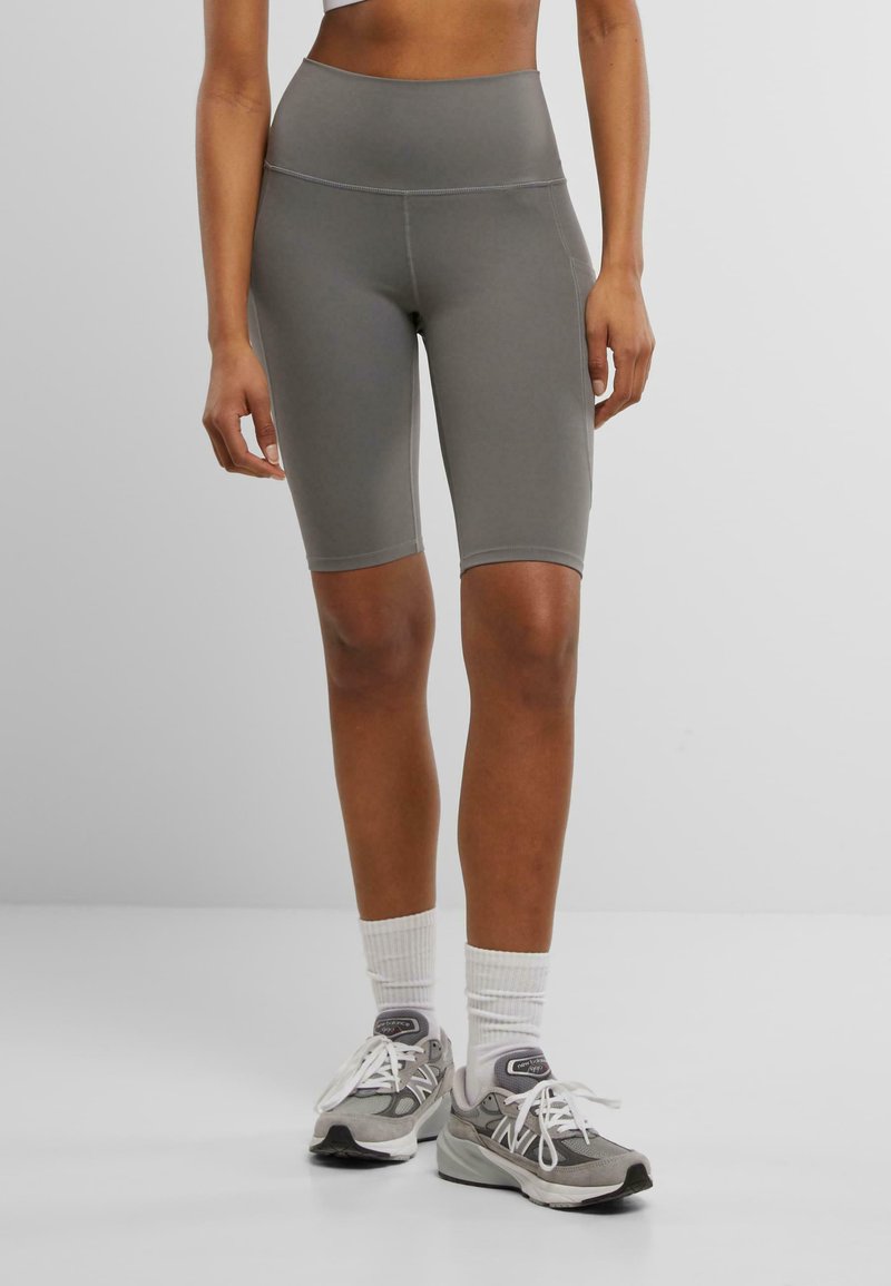 Graue, hoch taillierte Radshorts aus dehnbarem Material, mit glatter Textur und kontrastierenden Nähten. Kombiniert mit grauen Sneakers.