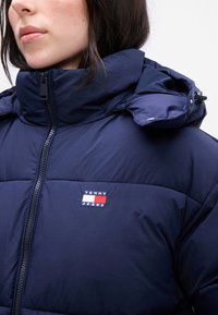 Ναυτικό φούτερ τζάκετ με ψηλό γιακά, διαθέτει φερμουάρ μπροστά και μικρό λογότυπο σε κόκκινο, λευκό και μπλε χρώμα με την ένδειξη "TOMMY JEANS."