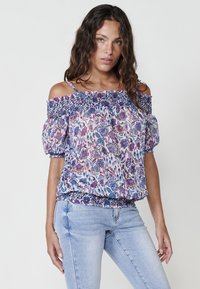 Blusa floreale scollata con scollatura e orlo arricciati, caratterizzata da motivi viola, blu e rosa su uno sfondo chiaro.