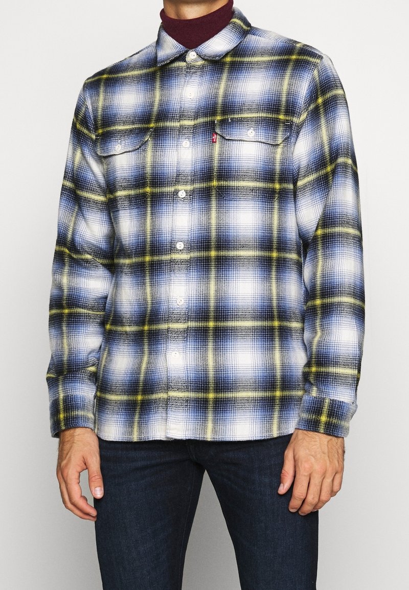 Camicia da uomo in flanella con un motivo a quadri blu, bianco e giallo, design a bottoni e due tasche sul petto. Tessuto morbido e maniche lunghe.
