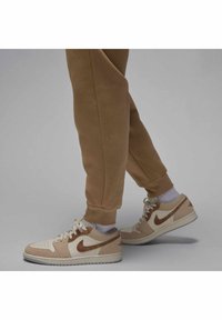 Beige Nike Air Jordan sneakers with tan suede accents, white mesh, and rubber soles. Worn with brown joggers and white socks.