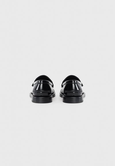 Ein Paar schwarze, glänzende Lederlofer, von hinten vor einem schlichten weißen Hintergrund gezeigt.