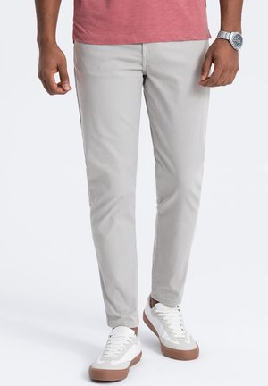 Chinos slim fit di colore grigio chiaro con una texture liscia. Abbinati a sneakers bianche con dettagli beige. Design semplice, senza motivi visibili.