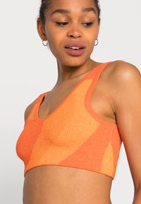 Bralette cropped em malha laranja com decote V profundo, alças largas e um padrão texturizado com formas geométricas. Material suave e elástico.