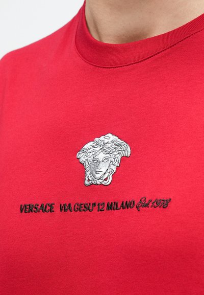 Κόκκινο βαμβακερό T-shirt με ασημί κεντημένο λογότυπο Medusa και το κείμενο "VERSACE VIA GESU' 12 MILANO Est. 1978" από κάτω.
