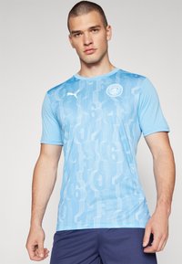T-shirt bleu clair à manches courtes avec un motif texturé de grands chiffres, logo PUMA et emblème de Manchester City sur la poitrine.