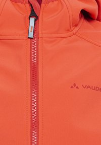 Orangene Jacke aus glattem Stoff, mit einem zentralen Reißverschluss und kontrastierenden roten Zähnen sowie einem Logo auf der linken Seite.