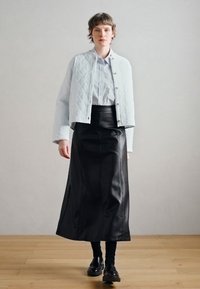 Világoskék steppelt dzseki, fehér galléros ing és fekete bőr hosszú szoknya. A dzsekin sima textúrák és fémes gombok találhatók.