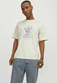 Cream-colored t-shirt with a relaxed fit, featuring a purple graphic print of a cartoon character with the text "I told you."