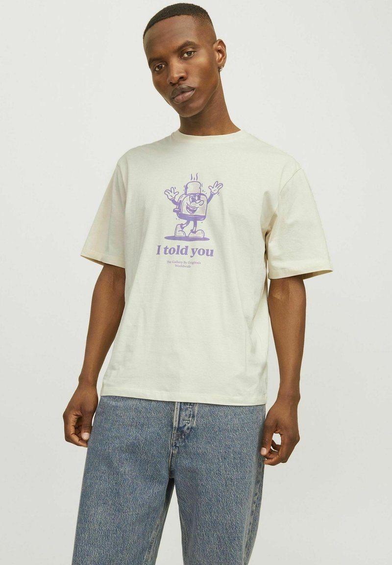 Cream-colored t-shirt with a relaxed fit, featuring a purple graphic print of a cartoon character with the text "I told you."