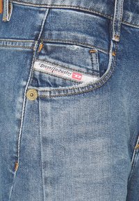 Denimjeans i ljusblått med blekta sektioner. Har en metallknapp, orange sömmar och en synlig varumärkesetikett på bakfickan.