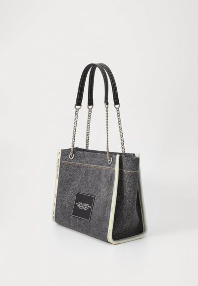 Sac fourre-tout en toile gris avec poignées en cuir noir et chaîne en argent. Présente un dessous blanc contrasté et un patch de logo à l'avant.