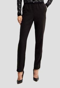 Pantaloni neri slim-fit realizzati in morbido tessuto, con una vita elastica e un sottile dettaglio laterale. Abbinati a scarpe con tacco alto nere.