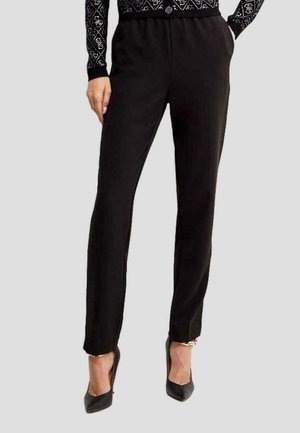 Pantaloni neri slim-fit realizzati in morbido tessuto, con una vita elastica e un sottile dettaglio laterale. Abbinati a scarpe con tacco alto nere.