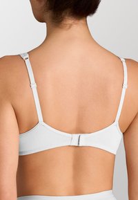 Reggiseno bianco con spalline regolabili, chiusura a gancio e occhiello e tessuto morbido. Il design sul retro presenta una finitura senza cuciture e una texture morbida.