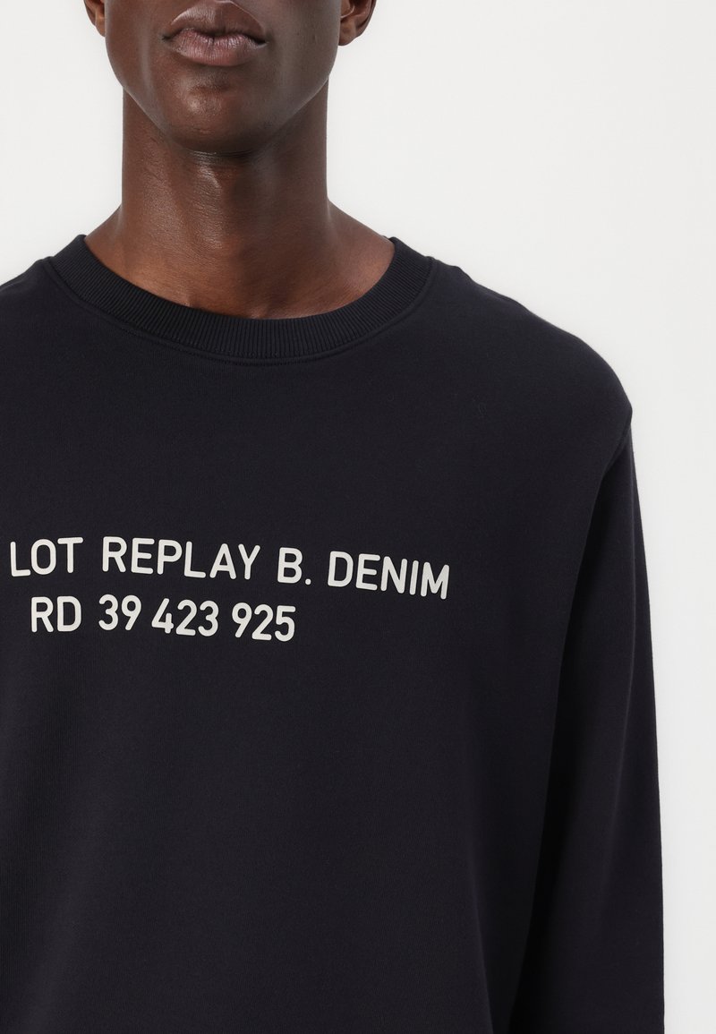 Le sweat-shirt marine présente un texte imprimé en blanc : "LOT REPLAY B. DENIM RD 39 423 925." Design classique à col ras du cou avec un col en bord-côte.