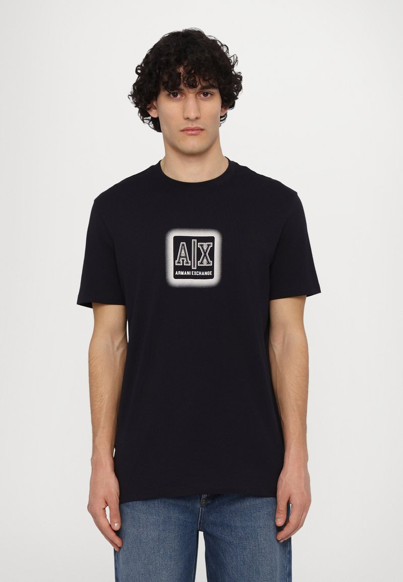 Camiseta de algodón negra con un gran logo blanco "A|X" y el texto "Armani Exchange". Cuello redondo, mangas cortas y un ajuste relajado.
