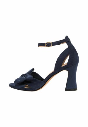 Marineblaue Wildleder-Pumps mit Knöchelriemen, Schnallenverschluss, geknotetem Vorderteil und geformtem Blockabsatz.