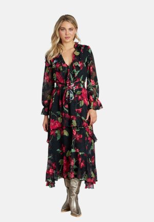 Abito maxi floreale in tessuto nero con stampe botaniche rosse e verdi, volants, maniche lunghe e vita cintrata. Abbinato a stivali metallici.