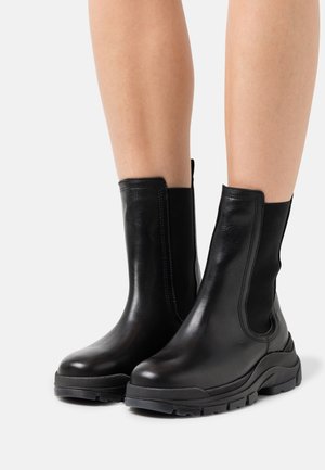 Black leather ankle boots with elastic side panels, round toe, and thick rubber soles, showcasing a smooth texture and streamlined design.