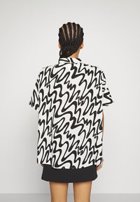 Košile s krátkými rukávy z lehké látky s černobílým abstraktním vlnkovým vzorem, volným střihem a mírně vroubkovaným lemem.