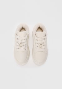 Baskets beige clair avec une tige en cuir lisse, doublure en fausse fourrure douce, accent avec un logo rond et semelles en caoutchouc texturé. Quatre œillets pour les lacets.