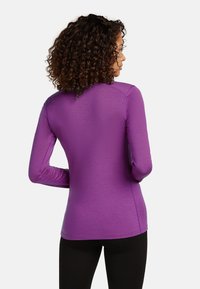 Lila långärmad topp med en figurnära design och platta sömmar, tillverkad av ett mjukt, stretchigt material, kombinerad med svarta leggings.