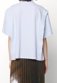 Jasnoniebieska, oversize koszulka z teksturowanej tkaniny, krótki rękaw, surowe brzegi i luźny krój, zestawiona z plisowaną, wielokolorową spódnicą.