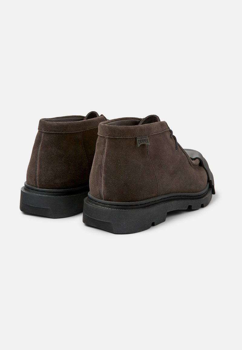 Braune Wildleder-Ankelboots mit einer abgerundeten Spitze, schwarzer Gummisohle und einem dezenten Logotag an der Seite. Glatte Textur mit minimalistischem Design.