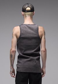 Γκρι αμάνικη μπλούζα με χαλαρή εφαρμογή, διαθέτει στρογγυλεμένο λαιμόκομμα και ίσιο τελείωμα. Το ύφασμα έχει διακριτική υφή.