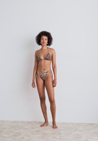 Bikini komplet z leopardskim vzorcem, ki vsebuje trikotni zgornji del in hlačke z visokim pasom. Mehka tkanina z vezalkami. Ozadje je enobarvne svetle barve.
