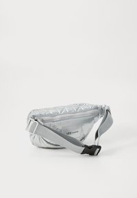 Sølv kviltet crossbody veske med glidelås lukking, med en grå justerbar stropp og et lite logomerke på siden.