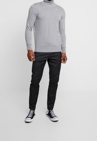 Szary sweter z golfem z dzianiny, zestawiony z czarnymi, dopasowanymi spodniami i czarno-białymi niskimi sneakersami.