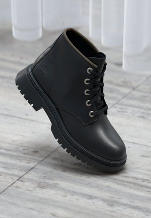 Black leather ankle boot with textured surface, round toe, rubber sole, and gold eyelets for laces, featuring a subtle logo detail.
