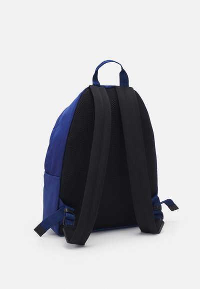 Blå nylonryggsäck med ett mesh-bakpanel, svarta vadderade remmar och justerbara sidspännen. Minimalistisk design med ergonomisk form.