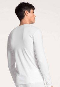 Long-sleeve white shirt made of a smooth, stretchy fabric, featuring a crew neck and fitted design, shown from the back.