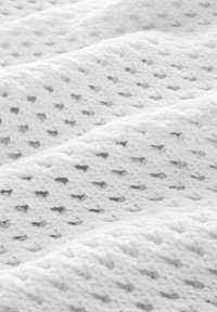 Blød hvid strikket stof med et tekstureret mønster af diagonale rækker og små åbne huller, vist i nærbillede med lys skygger.