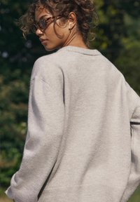 Maglione grigio chiaro a maglia con una vestibilità rilassata, spalle scese e polsini a coste. Il tessuto sembra morbido e strutturato.